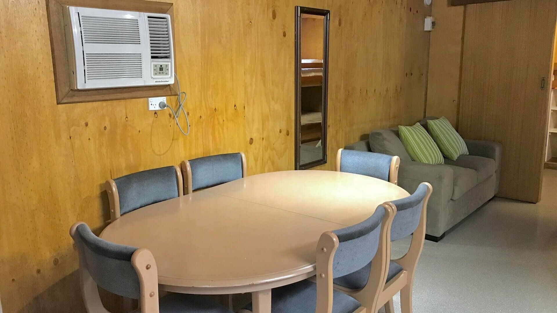 Una habitación con una mesa redonda y cuatro sillas, un sofá con cojines, y un aire acondicionado instalado en la pared.