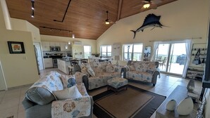 A spacious living area with a large sofa set, a dining table, and a kitchen in the background.