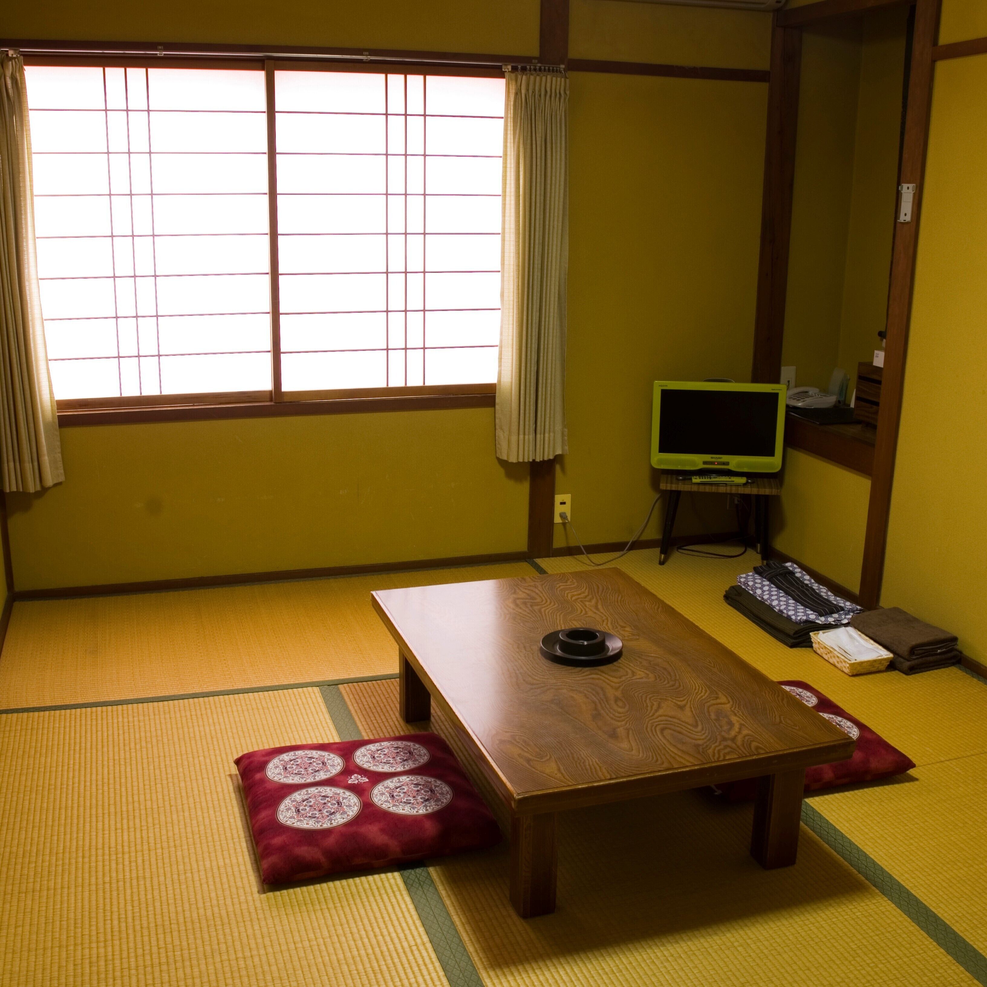 A traditional Japanese room with tatami flooring, a low wooden table, a television, and a desk with a keyboard.