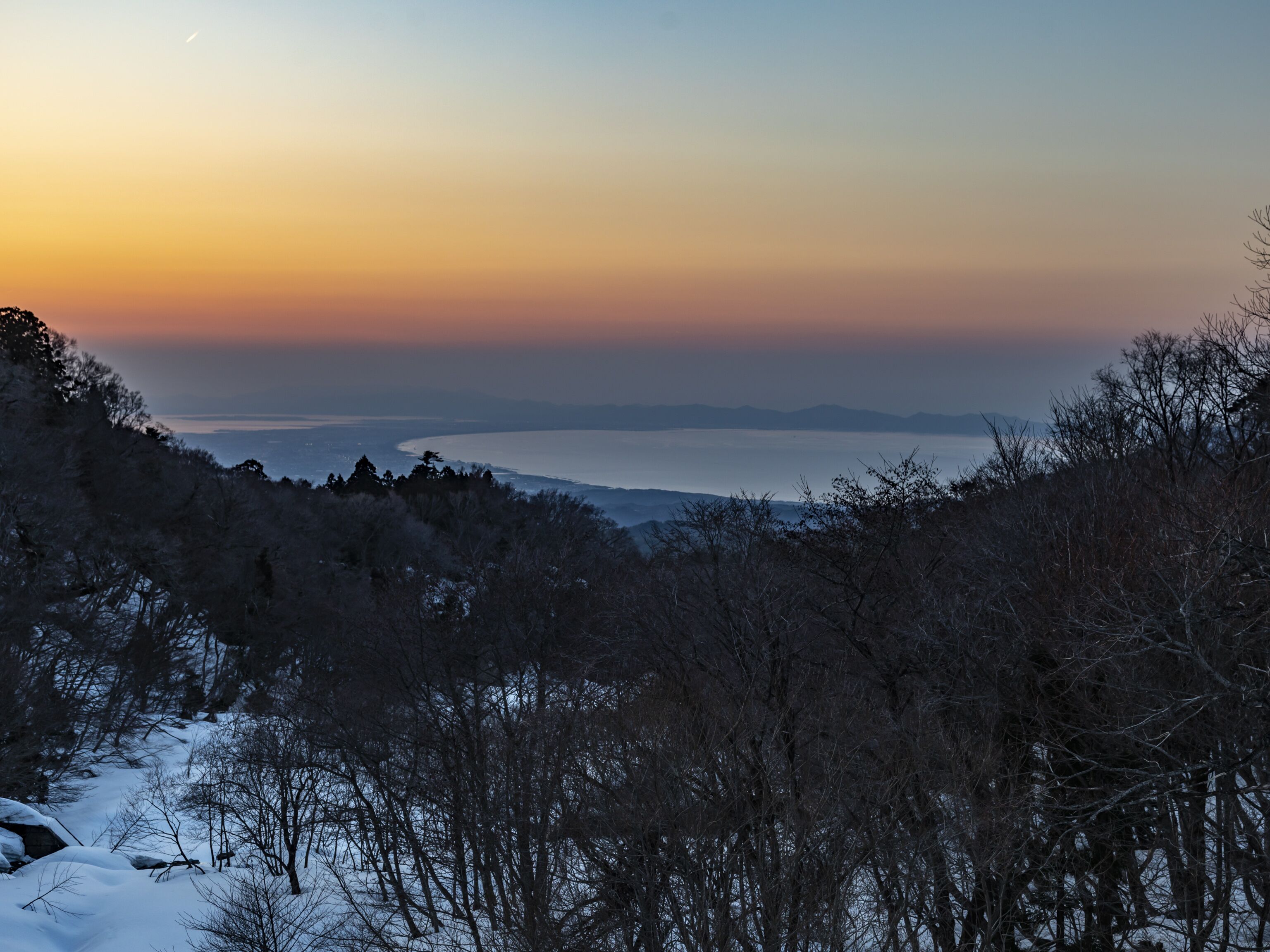 Een weids uitzicht op een kustlandschap tijdens zonsondergang, met besneeuwde gebieden en schaarse begroeiing.