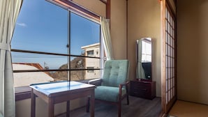 A room with a large window, a wooden table, a green chair, a small wooden cabinet, and a tatami mat. - Tabist Sekkasou (Daisen)