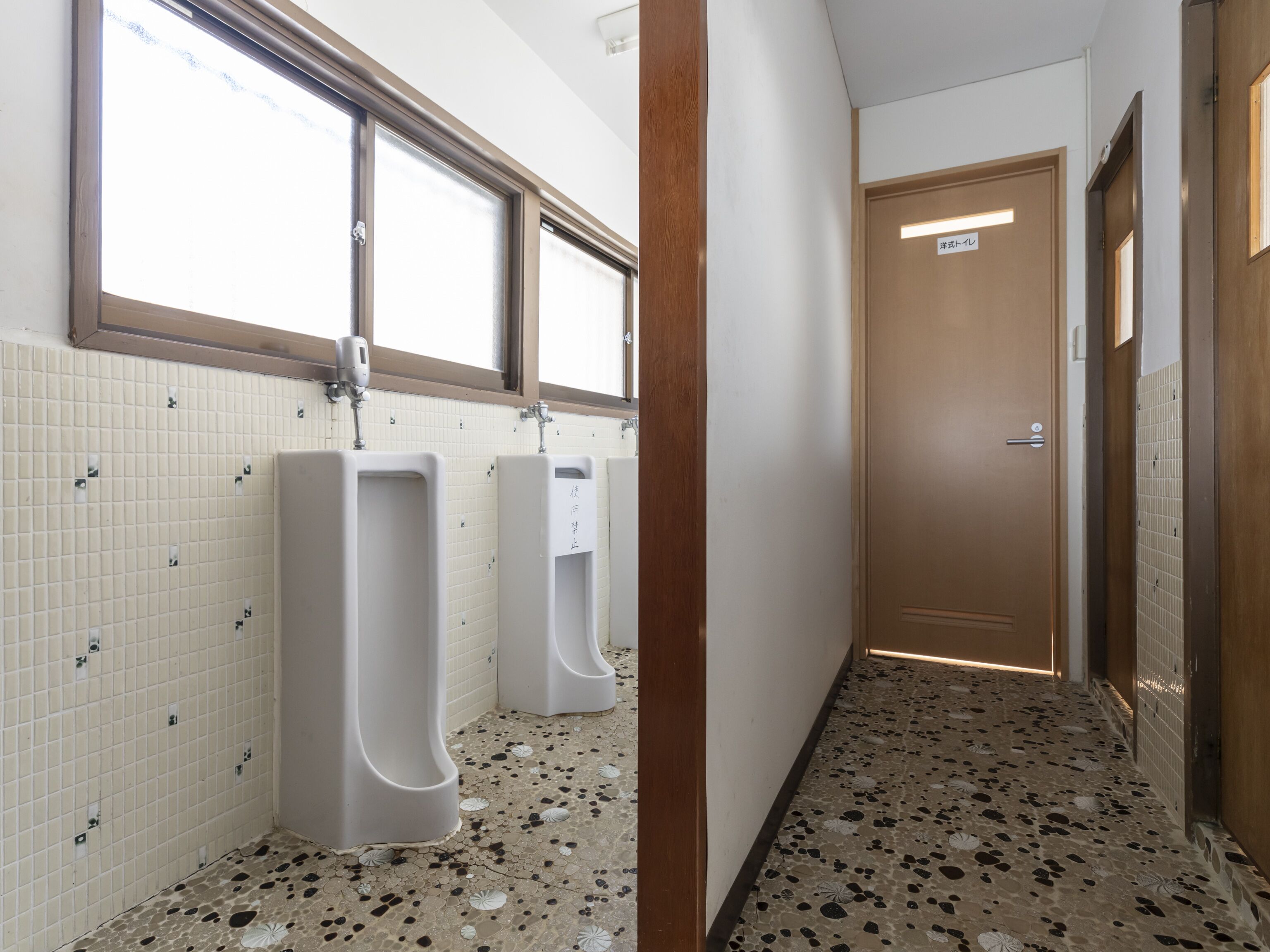 A men's restroom with two urinals, a tiled floor, and a door with a sign.