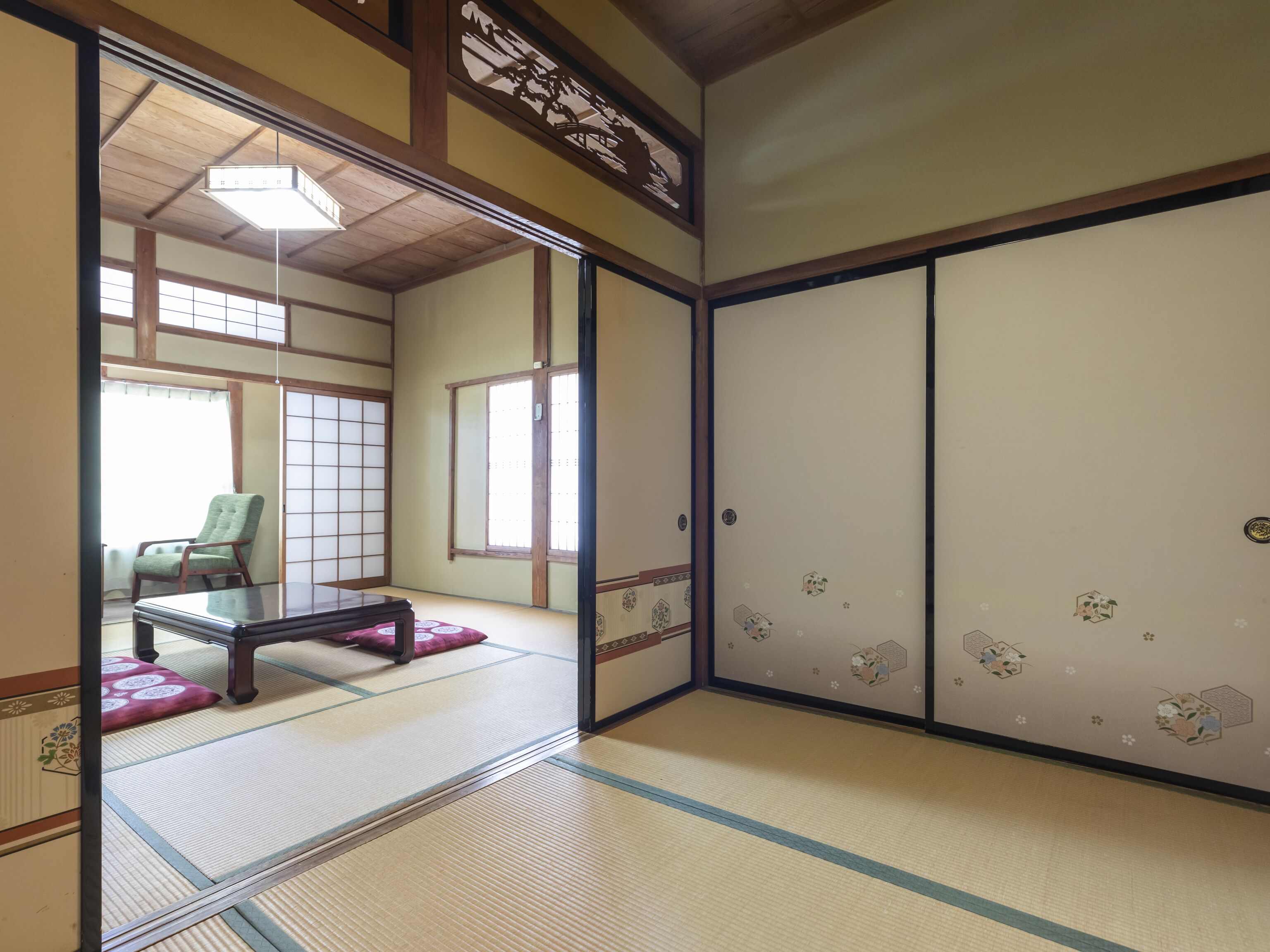 A traditional Japanese room with tatami flooring, a low table with a cushion, and sliding doors with floral patterns.