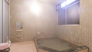 A bathroom with a large bathtub, a window, and tiled walls.