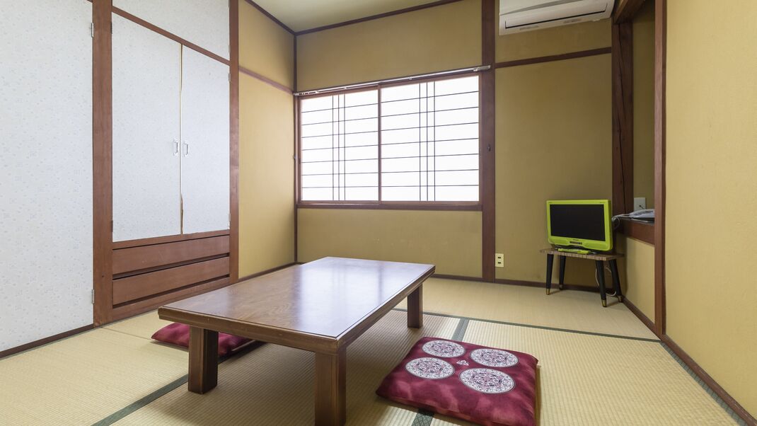 Een traditionele Japanse kamer met tatami vloerbedekking, een houten tafel, een televisie op een klein standaardje en schuifdeuren.