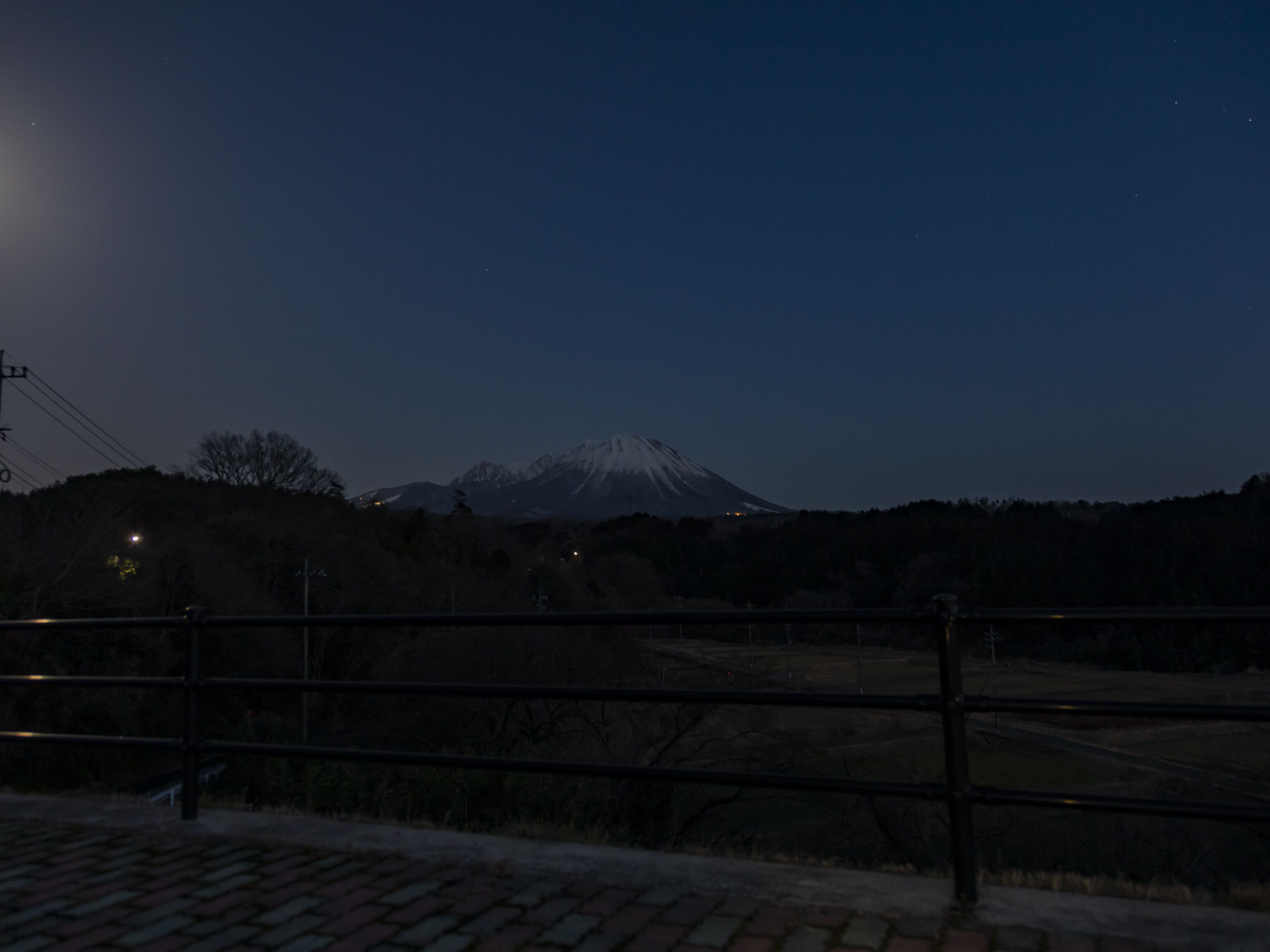 A view of a mountain at dusk with a fence in the foreground.