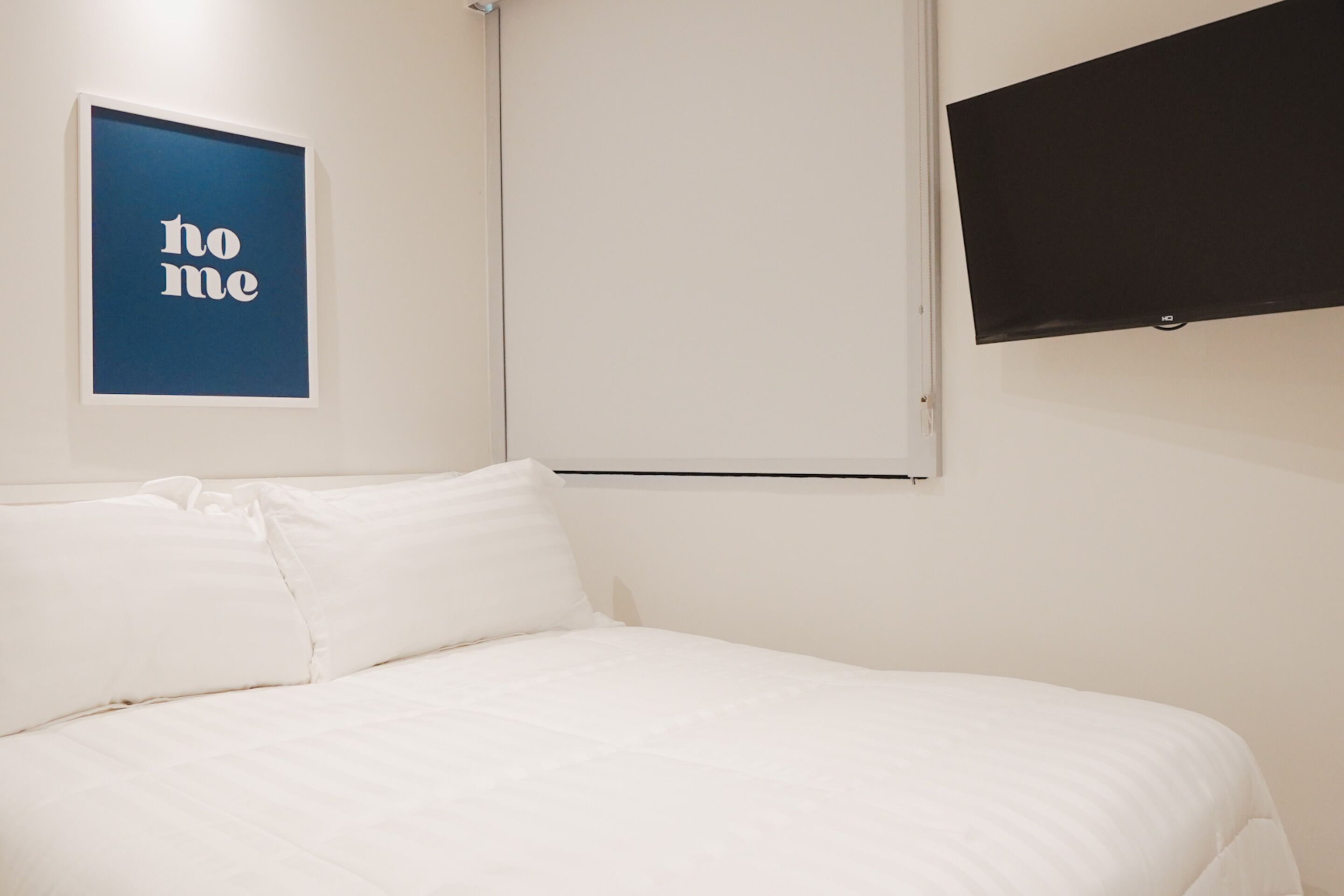 A bedroom with a bed, a wall-mounted TV, and a framed 'home' sign.