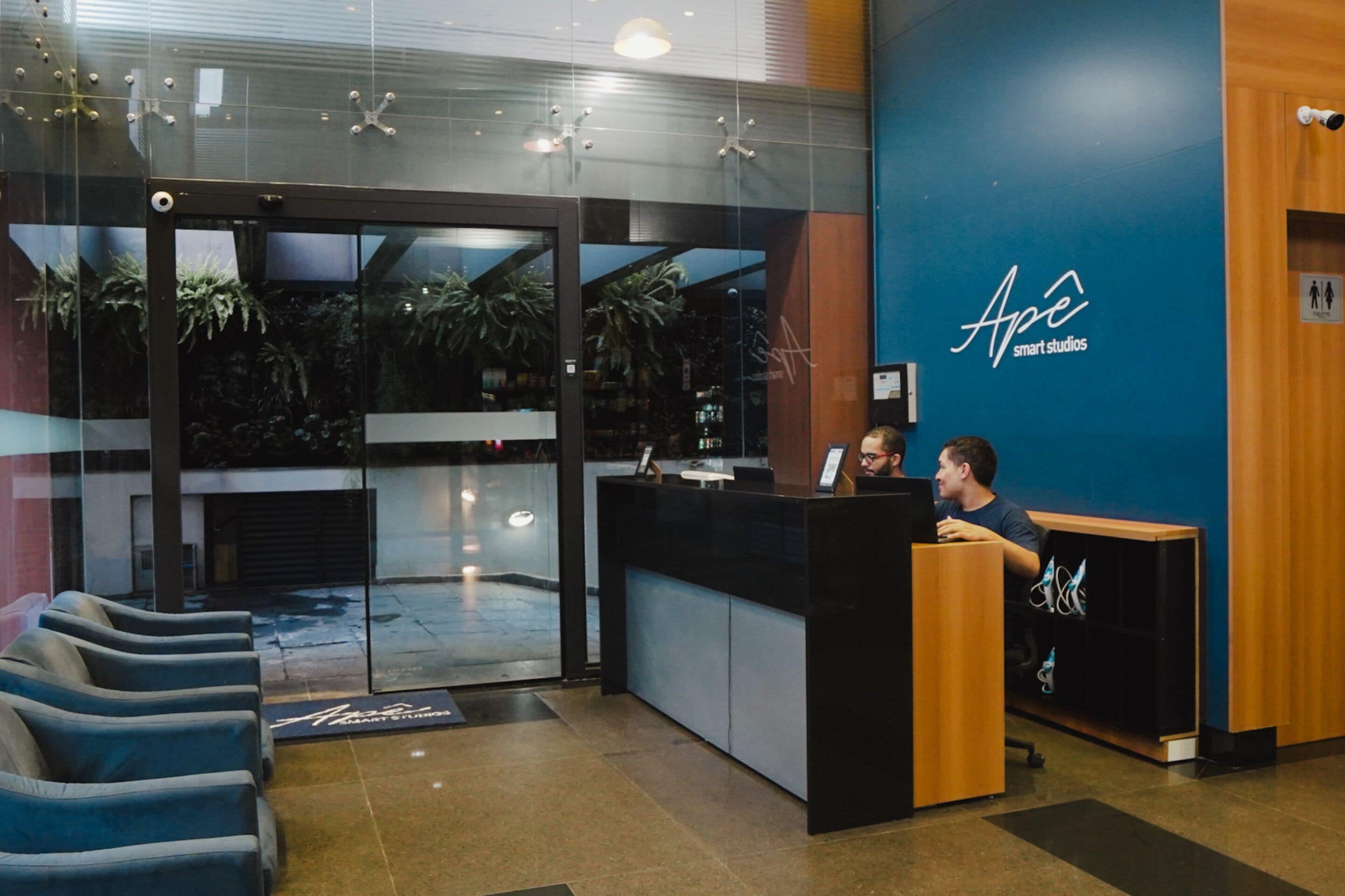 A reception area with a glass door entrance, a reception desk, and a blue wall with the logo "Ape smart studios".