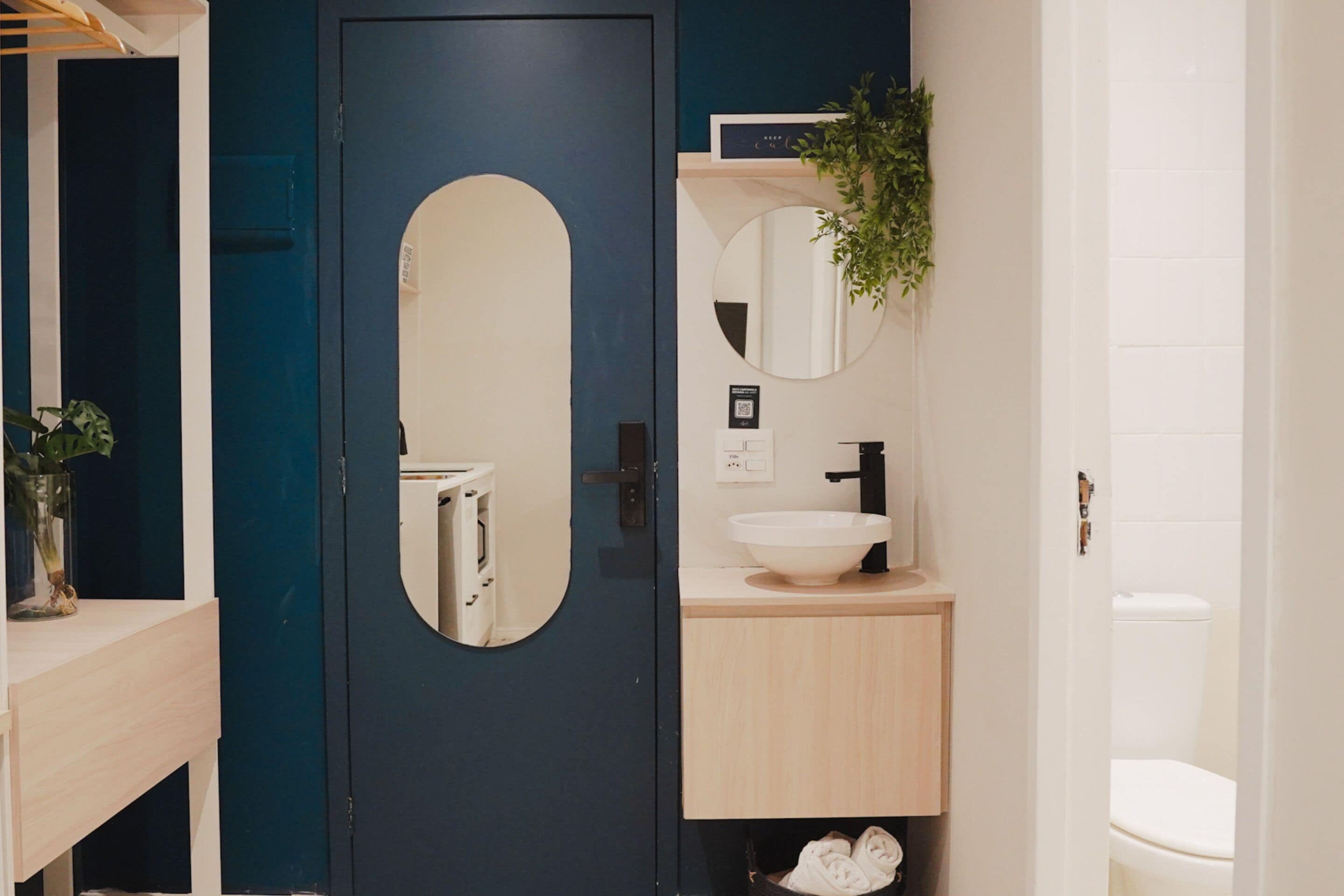 Un baño con una puerta azul oscuro, un lavabo blanco, un espejo y un inodoro.