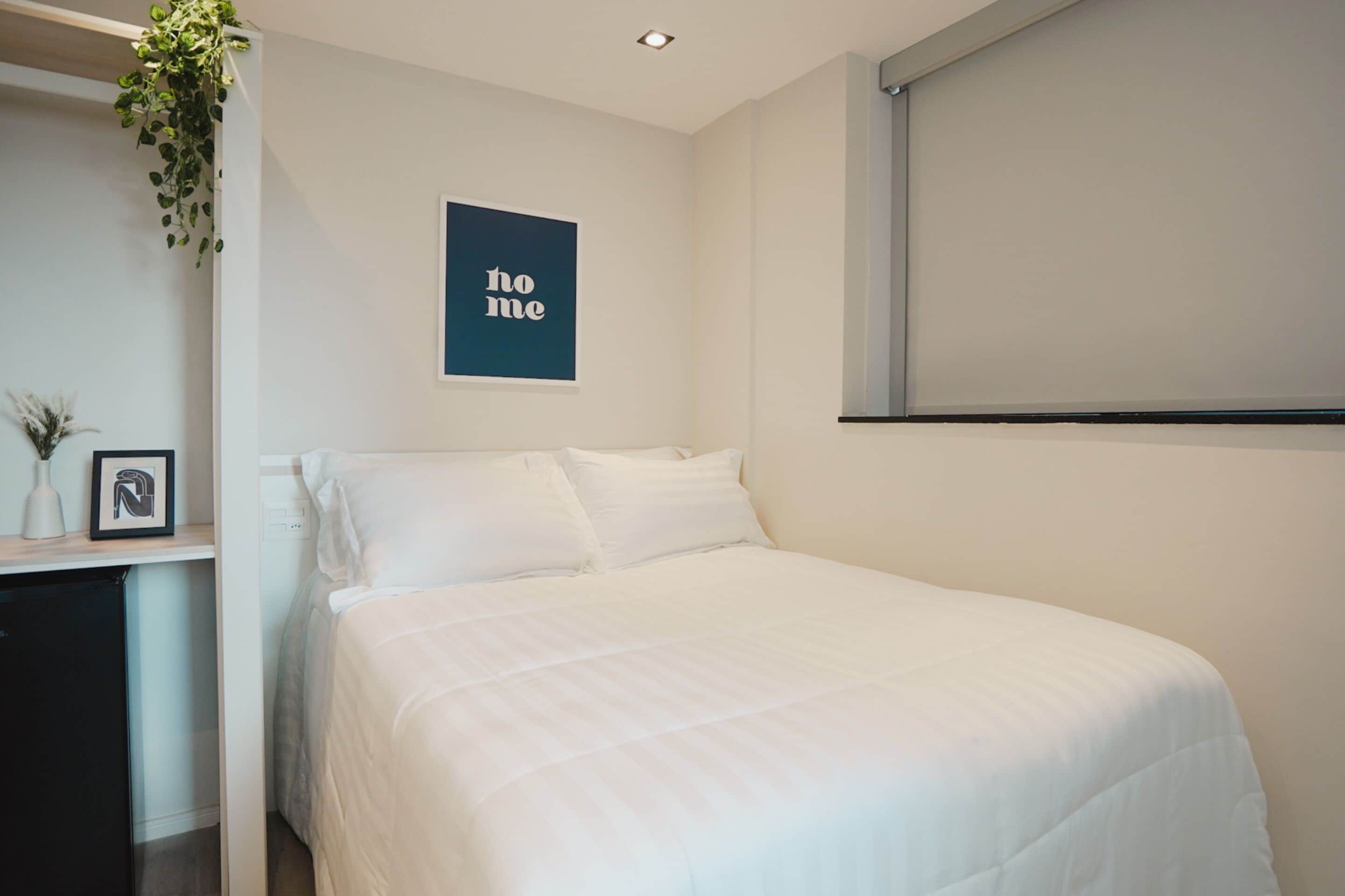A bedroom with a bed, a framed picture, a small table with a vase, and a 'home' sign on the wall.