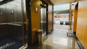 A hotel lobby with a shiny floor, a trash bin, and an elevator.