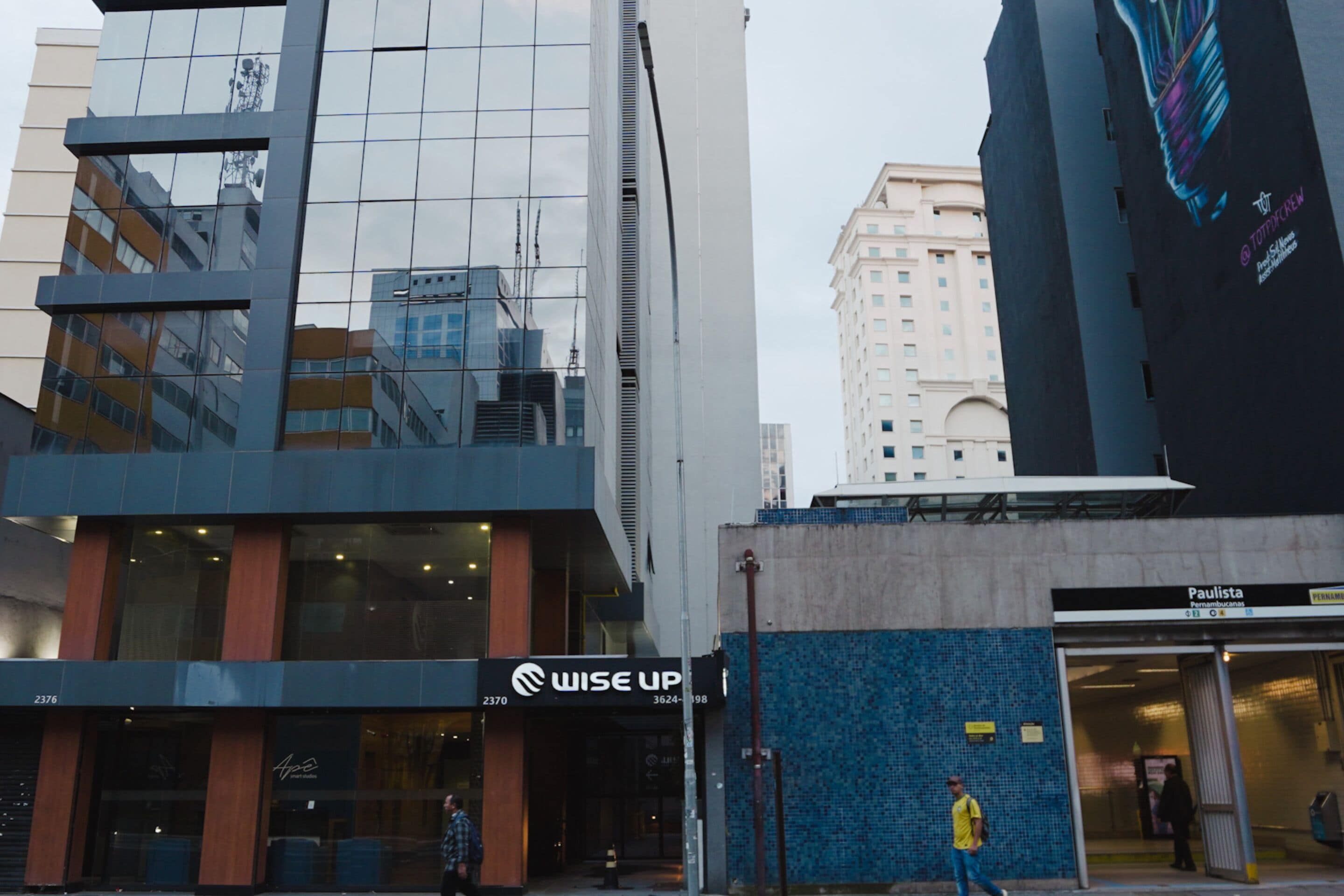 Un edificio moderno con fachada de vidrio, un escaparate visible con un letrero que dice “WISE UP” y una pared de azulejos azules.