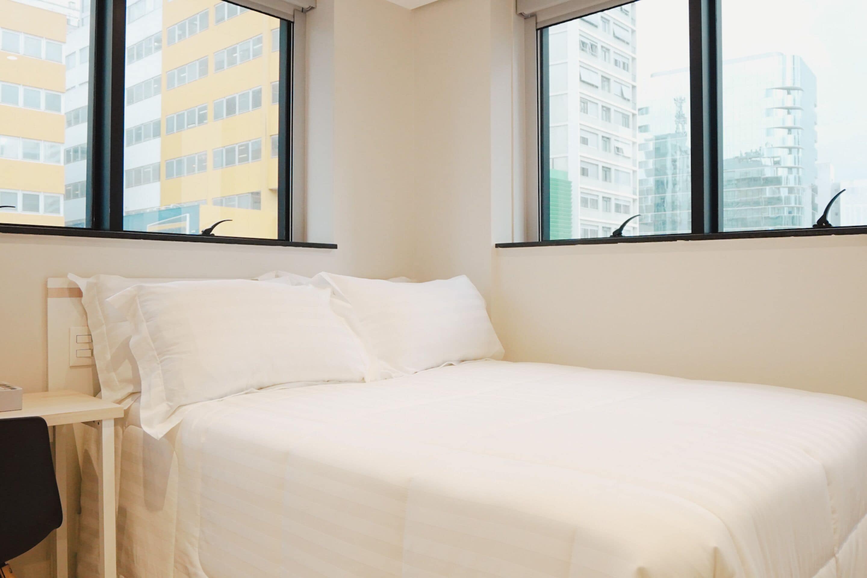 Une chambre à coucher avec un lit, une chaise et une fenêtre donnant sur des immeubles.
