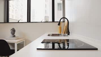 Una cucina moderna con piano cottura a induzione nero, un bancone bianco e una finestra con vista sugli edifici.