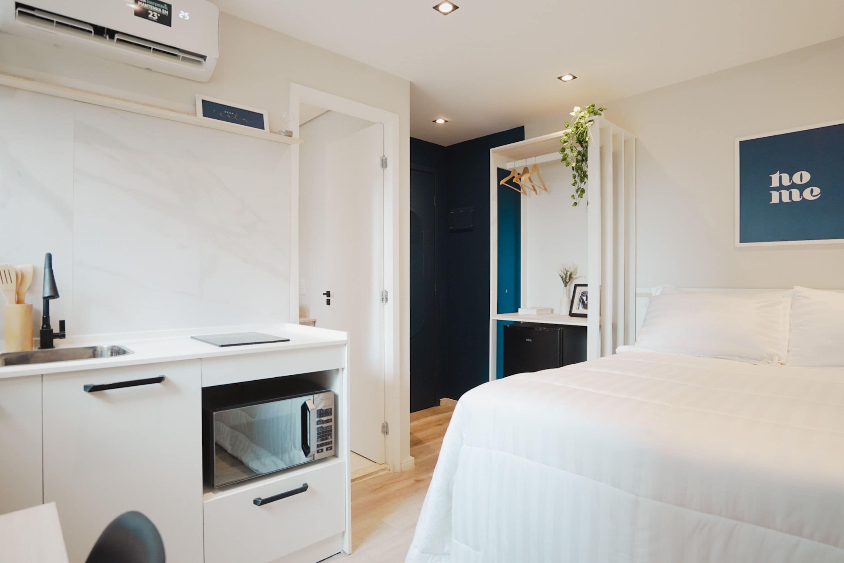 Ein modernes Schlafzimmer mit Bett, einer kleinen Küchenzeile mit Mikrowelle und einer wandmontierten Klimaanlage.