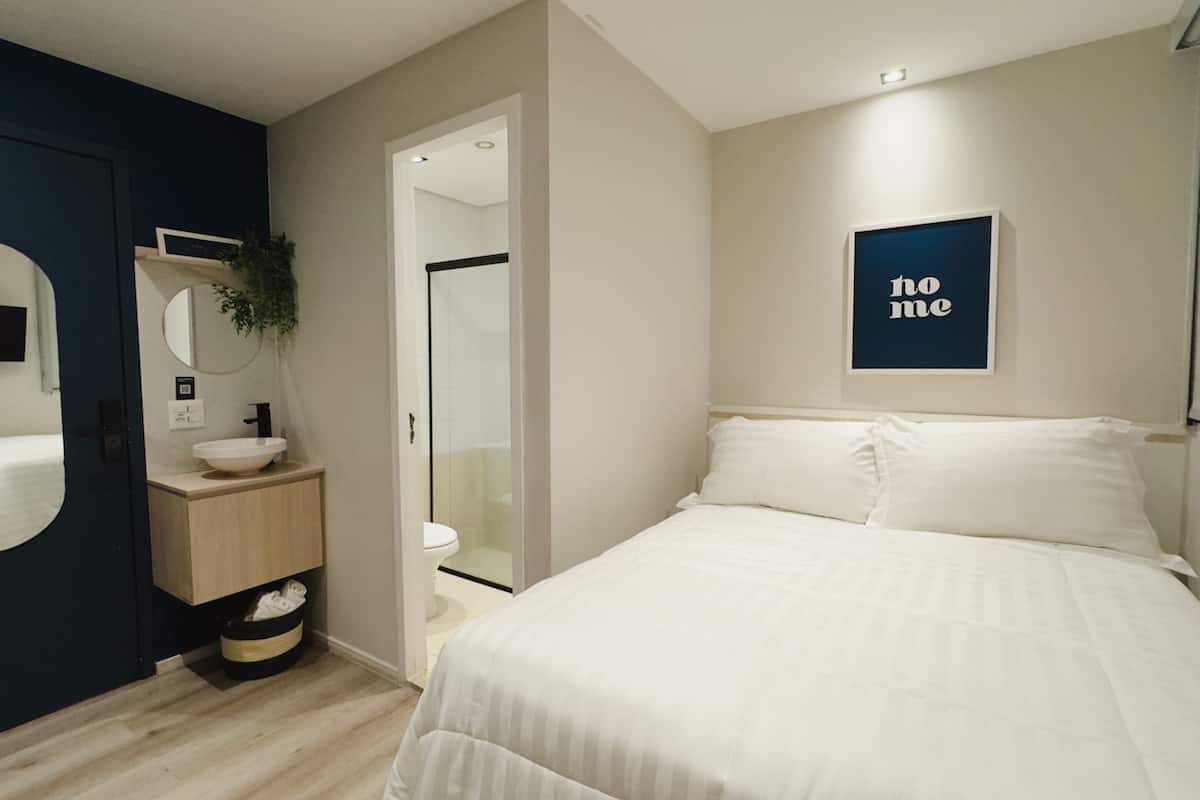 Un dormitorio moderno con una cama grande, una mesita de noche, un espejo montado en la pared y un letrero enmarcado.