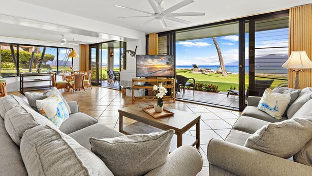 A spacious living room with a large TV, comfortable seating, and a view of a golf course. - Premier Spacious Condo with Stunning Ocean Views (Lahaina)