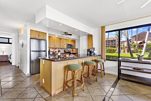 Une cuisine moderne dotée d’un îlot central, de meubles en bois, d’appareils électroménagers en acier inoxydable et d’une grande fenêtre donnant sur un espace paysager aménagé.