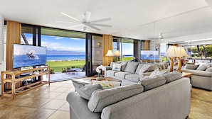 A modern living room with a large TV, comfortable seating, and a view of the ocean. - Premier Spacious Condo with Stunning Ocean Views (Lahaina)