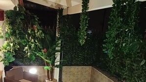 Uma área de estar aconchegante ao ar livre, com piso de pedra, cercada por plantas verdes exuberantes e uma parede escura.
