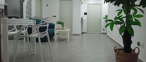 Ein modernes Wohnzimmer mit Essbereich, einer großen Topfpflanze und einer Küche im Hintergrund.