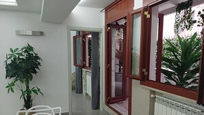 Uma sala de jantar com uma mesa posta para dois, uma planta em vaso e vista pela janela com moldura vermelha.