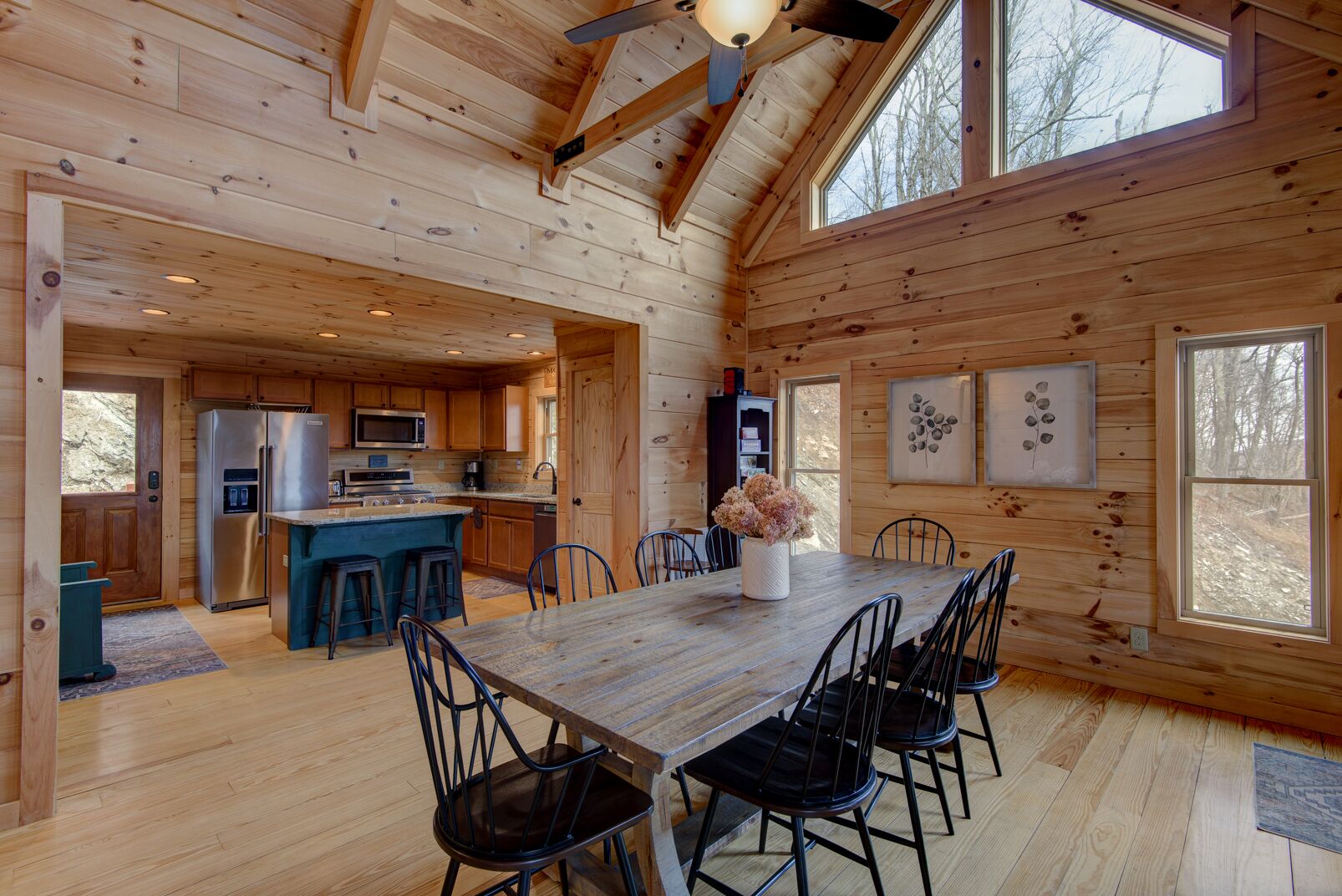 A spacious wooden cabin with a large dining table, kitchen area, and multiple windows.