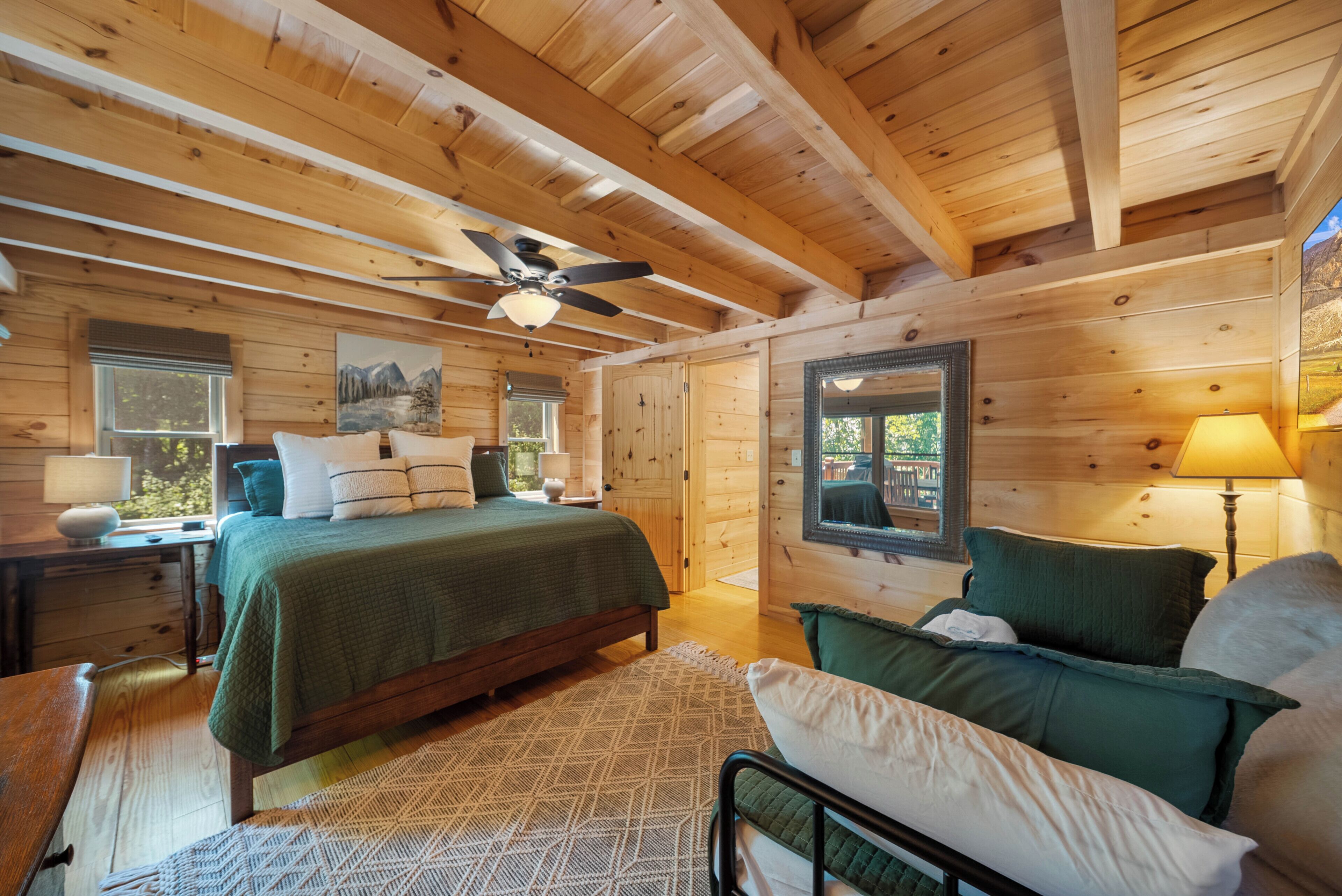 Une chambre dans une cabane en bois, comprenant un lit, une chaise, un bureau, un miroir et un ventilateur de plafond.