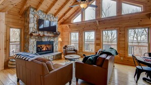 Un intérieur de chalet chaleureux avec une cheminée en pierre, des murs en bois et de grandes fenêtres.