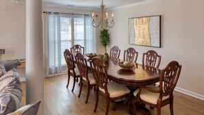 Une salle à manger avec une table ronde en bois, six chaises, un lustre et un grand tableau abstrait accroché au mur.