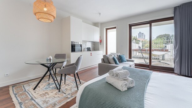 A modern hotel room with a large bed, a glass dining table, a kitchenette, and a balcony with a view. - GuestReady - Almada 516 Stay (Porto)
