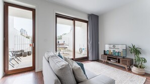 A modern living room with a sofa, TV, and a view of an outdoor patio. - GuestReady - Almada 516 Stay (Porto)