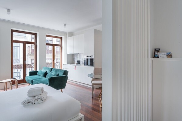 Una habitación de hotel moderna con cama, un sofá color turquesa, una mesita y una kitchenette.