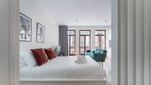 A modern hotel room with a large bed, a green armchair, and a view of the city through large windows. - GuestReady - Almada 516 (Porto)