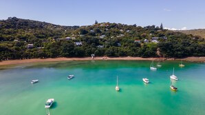 A coastal area with clear turquoise waters, several boats anchored, and a hillside with houses. - Koi Waiheke with private beach access (Waiheke Island)