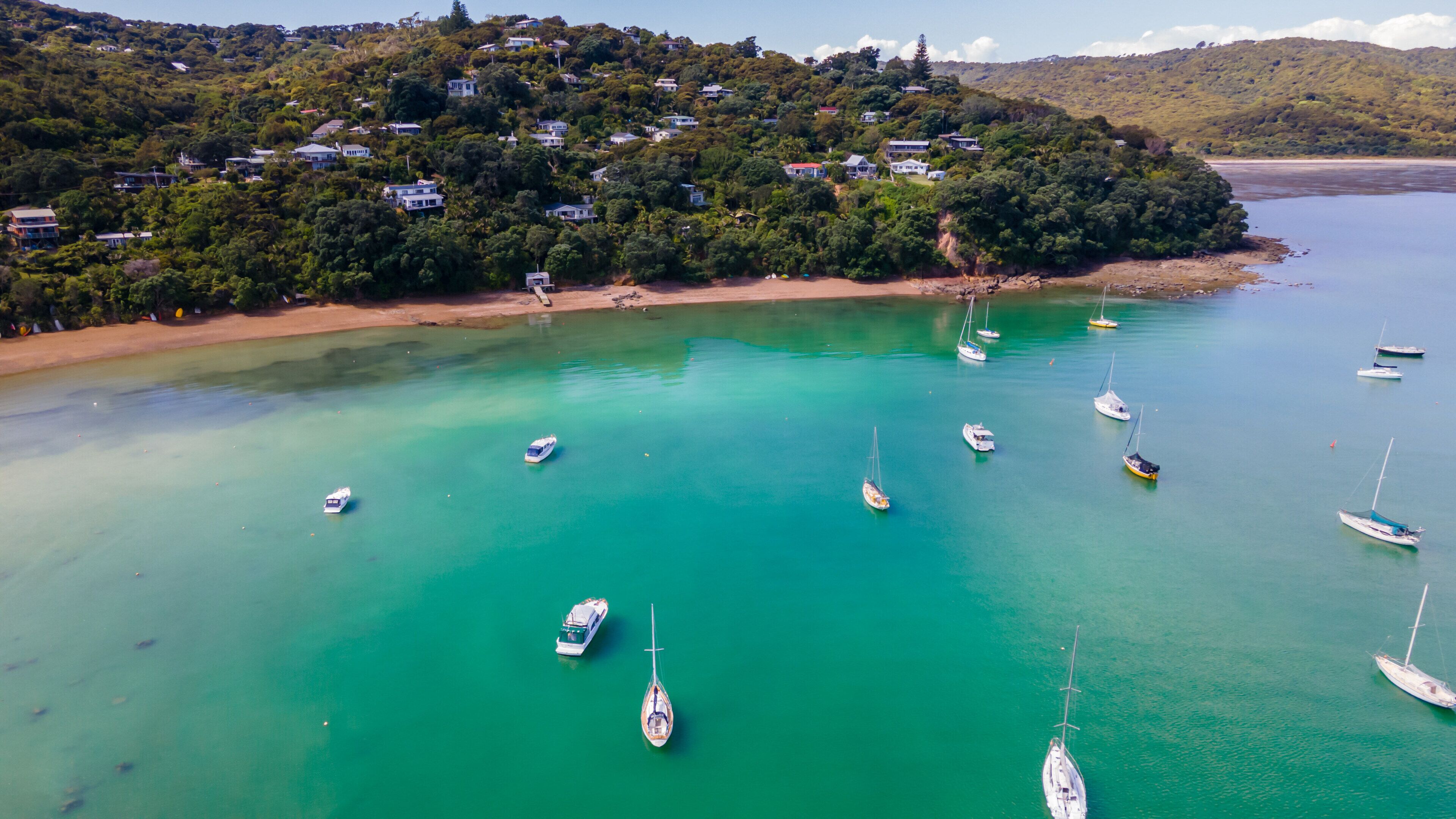 A coastal area with houses on a hillside and several boats anchored in turquoise waters.