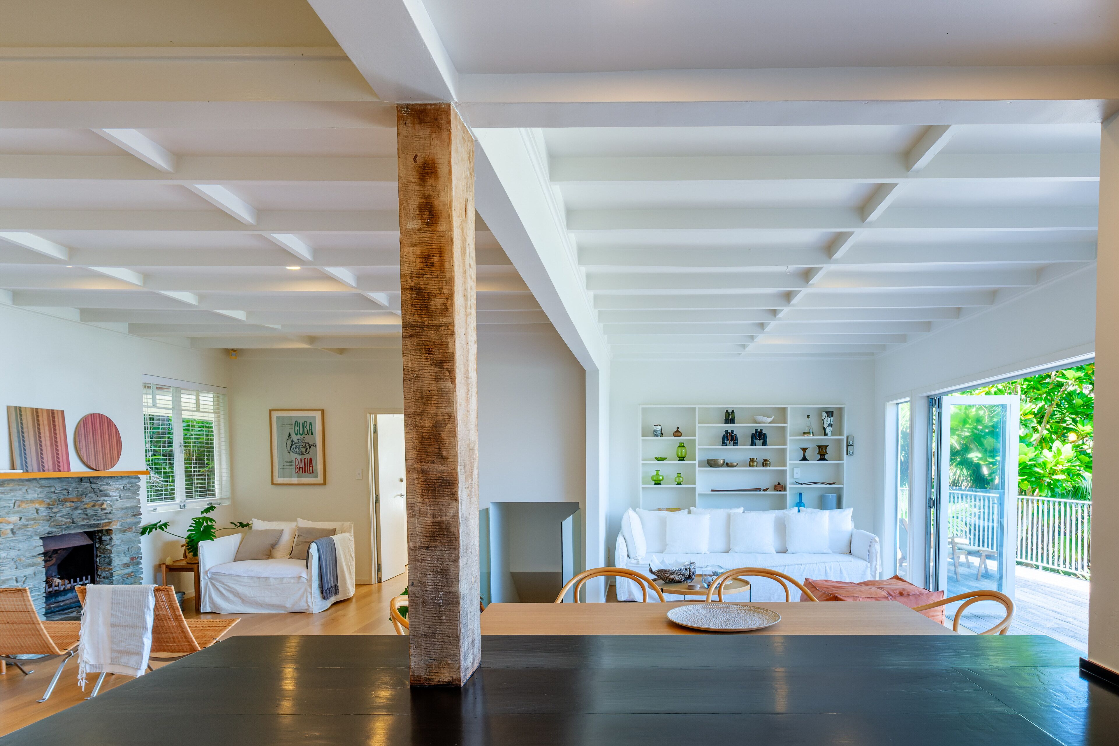 A spacious living room with a fireplace, a dining area with a table and chairs, and a view of a balcony with greenery.