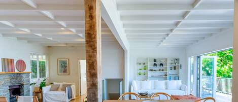 A spacious living room with a fireplace, a dining area with a table and chairs, and a view of a balcony with greenery.