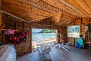 Una cabaña de madera con vista a la playa, un muelle y un bote.