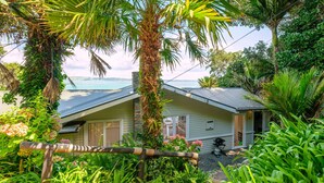 A house with a view of the ocean, surrounded by lush greenery and a wooden fence. - Koi Waiheke with private beach access (Waiheke Island)