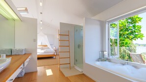A modern bathroom with a large window, a bathtub, and a shower area. - Koi Waiheke with private beach access (Waiheke Island)
