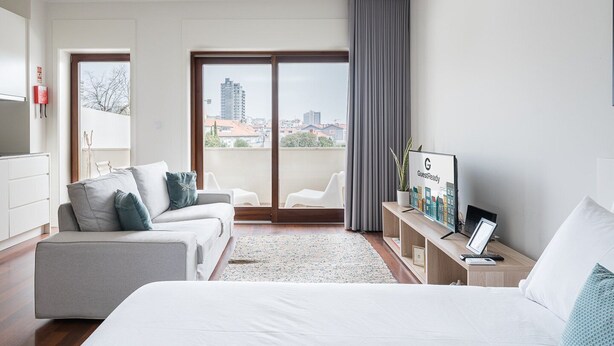 A modern hotel room with a large bed, two sofas, a TV, and a balcony with city views. - GuestReady - Almada 516 (Porto)