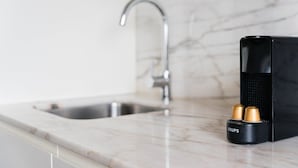 A kitchen with a marble countertop, a stainless steel sink, and a black coffee maker with two gold capsules. - GuestReady - Almada 516 (Porto)