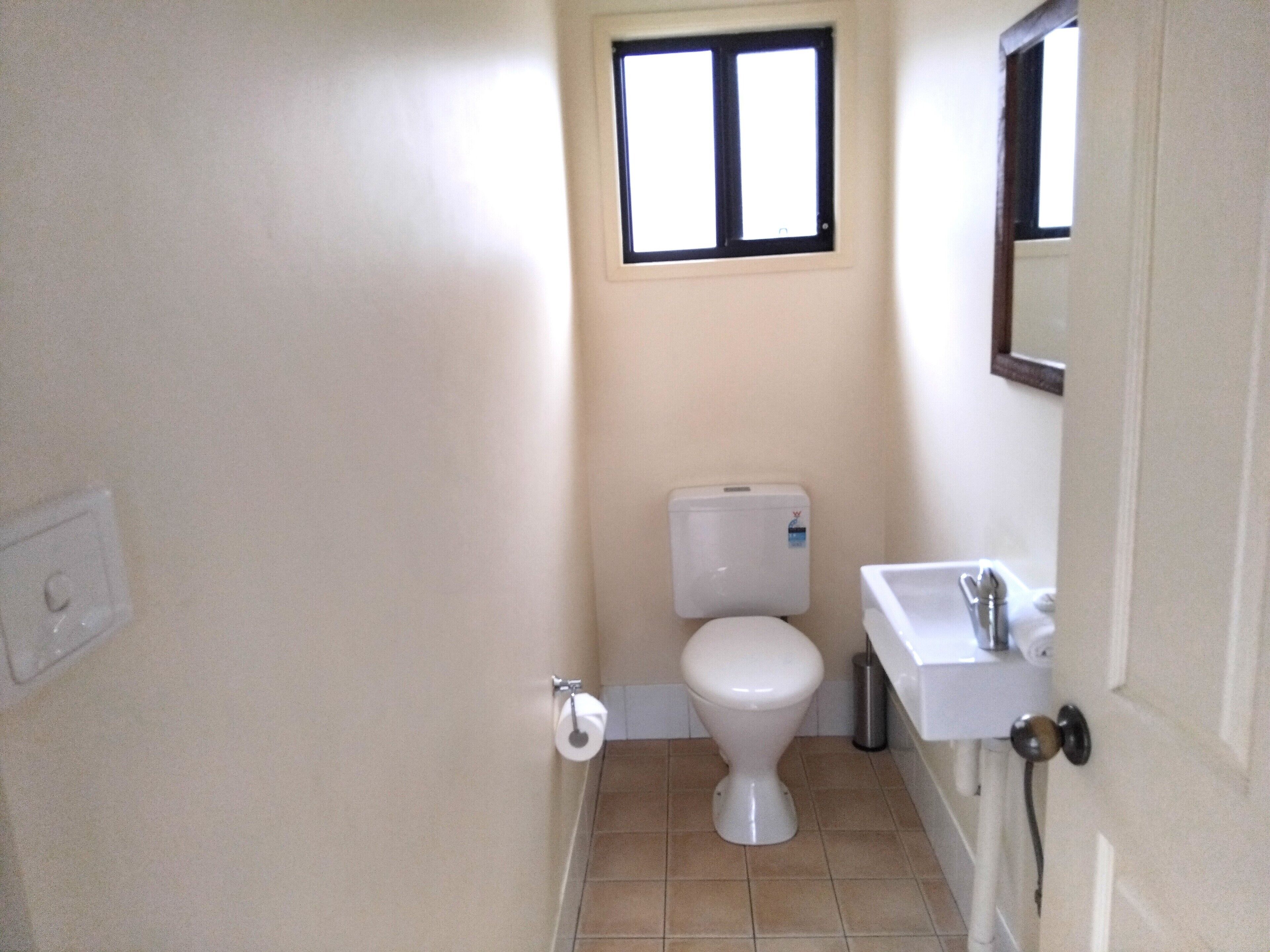 Ein kleines Badezimmer mit Toilette, Waschbecken, Fenster und Spiegel.