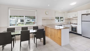 A modern kitchen with a central island, white cabinetry, and a large window overlooking a trailer park. - Shoalhaven Heads Village (Shoalhaven Heads)