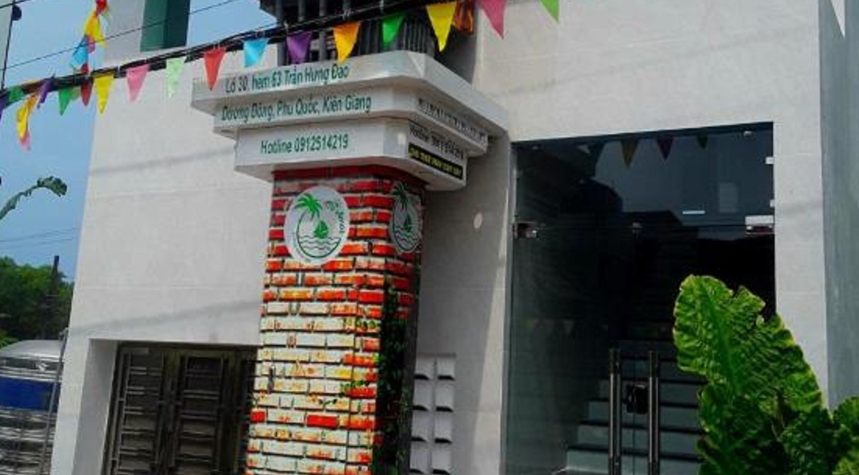 A building with a brick pillar featuring a logo and a signboard with text.
