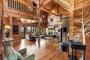 Een ruime cabin met een hoge plafond, houten wanden, een open haard, een eethoek en uitzicht op de natuur.