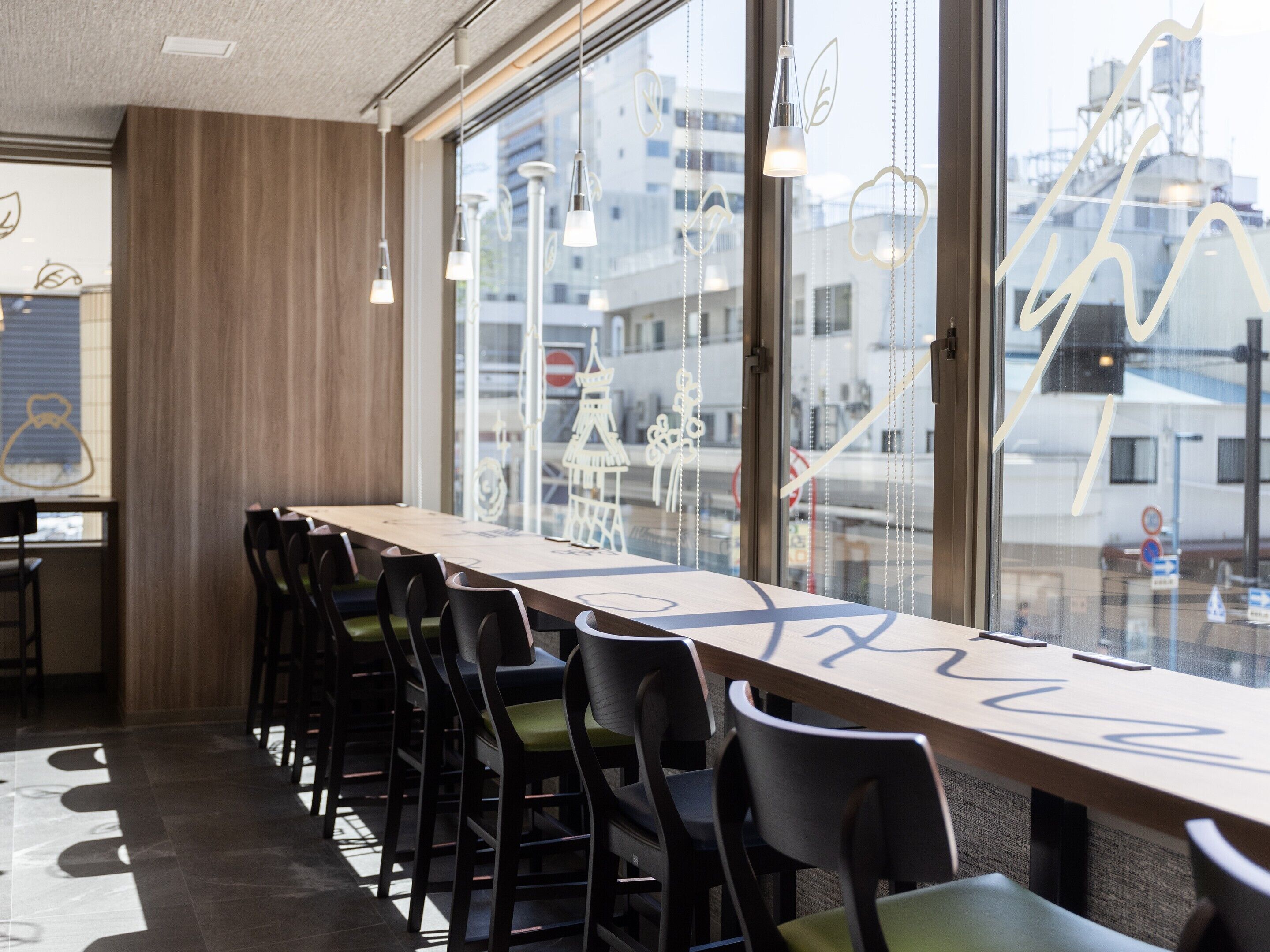 A conference room with a long table and chairs, large windows with city views, and hanging pendant lights.