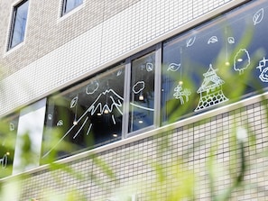 Fachada de edificio con revestimiento de baldosas y grandes ventanales que muestran dibujos lineales en blanco de montañas, nubes y un pagodas.