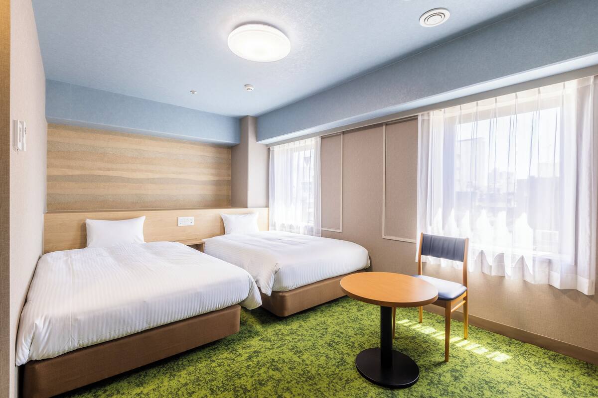 A hotel room with two beds, a small table, and a chair.
